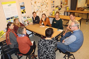 Eine Gruppe von Menschen sitzt an einem Tisch in der Ideenwerkstatt der um:welt und tauscht sich zu einem Thema aus.